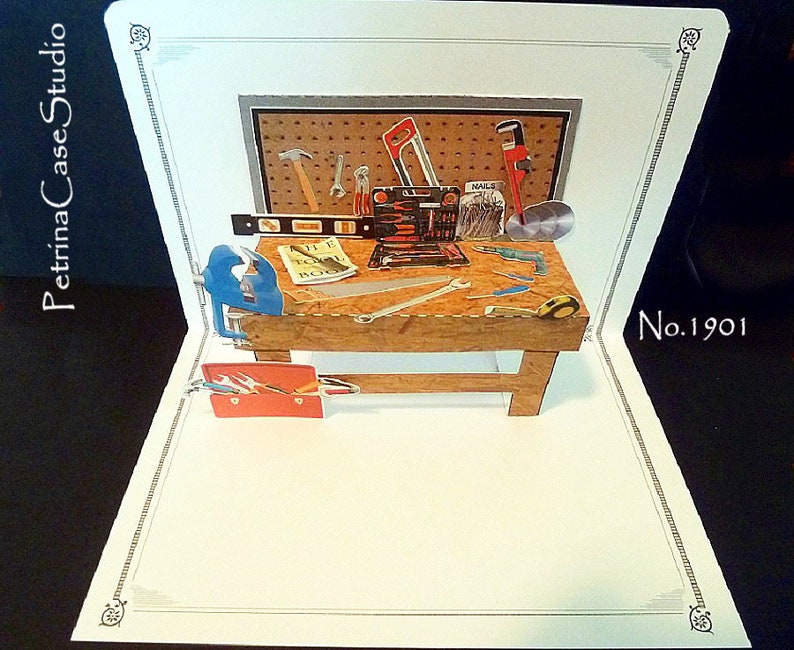 May include: A pop-up card depicting a wooden workbench with various tools, including a hammer, saw, wrench, level, and nails. The card is decorated with a gray and brown pegboard and a red toolbox. The card is labeled "No. 1901".