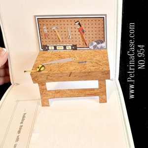 May include: A pop-up card with a wooden workbench and tools. The workbench has a saw, a tape measure, and a level. The tools are hanging on a pegboard. The card says "building things with us..." on the front.