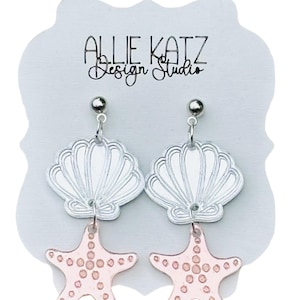 May include: Silver seashell earrings with pink starfish charms. The earrings are hanging from a silver ball stud. The earrings are displayed on a white card with the text "Allie Katz Design Studio".