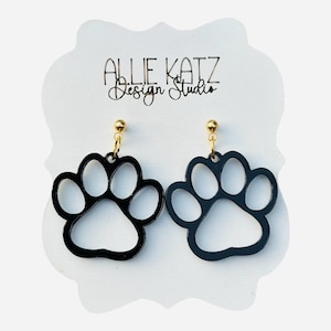 May include: Black paw print earrings with gold-colored ear wires. The earrings are displayed on a white card with the text "ALLIE KATZ Design Studio" in black script.