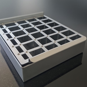 May include: A rectangular silver metal baking tin featuring a removable grid insert. The insert is constructed from intersecting metal strips secured with small screws, creating a uniform pattern of square compartments for even portioning.