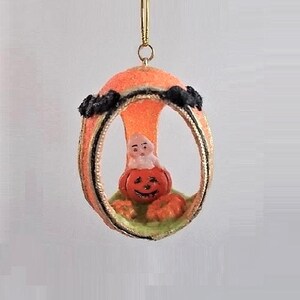 May include: A Halloween ornament featuring a ghost sitting inside a carved pumpkin. The ornament is made from orange and green felt and has a gold trim.