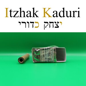 Puede incluir: La imagen presenta el texto "Itzhak Kaduri" en ingl&eacute;s y hebreo. Un objeto peque&ntilde;o y rectangular envuelto en papel y un objeto cil&iacute;ndrico est&aacute;n en primer plano sobre un fondo verde.