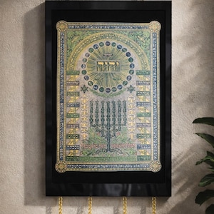 Op de afbeelding: Ingelijst kunstwerk met een zwarte rand, met een gedetailleerde, kleurrijke illustratie met Hebreeuwse tekst en symbolen. Het kunstwerk heeft een gouden ketting om op te hangen en decoratieve gouden accenten.