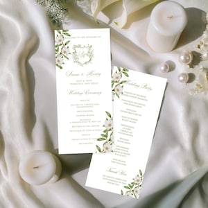 以下が含まれることがあります： 白いウェディングセレモニープログラム2つ。花柄のアクセントとテキストが特徴です。「Diana & Henry」の名前、結婚式の詳細、セレモニーの順番が含まれています。白いキャンドルと真珠も表示されています。