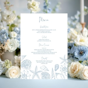 May include: A wedding menu card with a blue seashell border and elegant script. The menu includes appetizers, salad, main course, and dessert options. The card is surrounded by white and blue flowers.