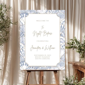 Peut inclure: Panneau de bienvenue de mariage avec le texte "Welcome to The Night Before Celebrating Jennifer & William". Le panneau a un fond blanc avec une bordure de coquillages bleus et dorés. Il est affiché sur un chevalet en bois.