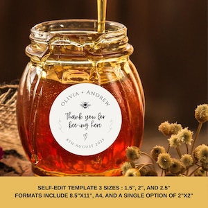 Puede incluir: Una pegatina redonda blanca con texto negro que dice "Olivia + Andrew Thank you for bee-ing here 8th August 2025" con un pequeño gráfico de abeja. La pegatina está en un tarro de miel.