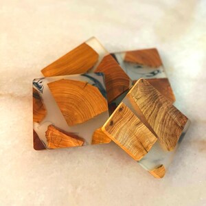 Op de afbeelding: Vier vierkante houten onderzetters met een transparante epoxyhars top. De onderzetters hebben een natuurlijk houtnerfpatroon en zijn lichtbruin.
