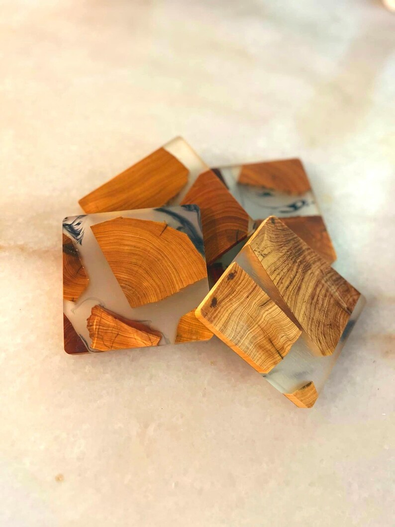 Op de afbeelding: Vier vierkante houten onderzetters met een transparante epoxyhars top. De onderzetters hebben een natuurlijk houtnerfpatroon en zijn lichtbruin.