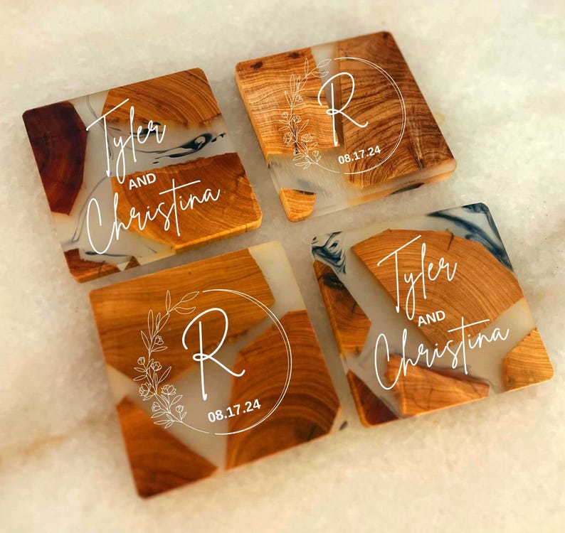 Op de afbeelding: Vier vierkante houten onderzetters met een transparante epoxyhars top. De onderzetters hebben een wit swirl-ontwerp en de namen "Tyler en Christina" en de letter "R" met de datum "08.17.24".