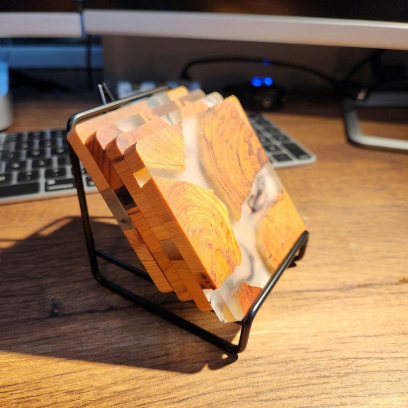 Op de afbeelding: Set van vier houten onderzetters met een transparant epoxyharsontwerp. De onderzetters zijn gestapeld en worden getoond op een zwarte metalen standaard.