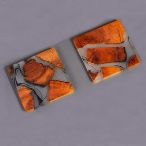 Op de afbeelding: Twee vierkante onderzetters gemaakt van hout en hars. De onderzetters hebben een lichtgrijze harsbasis met ingebedde bruine houten stukken. De houten stukken hebben een natuurlijke houtnerf.