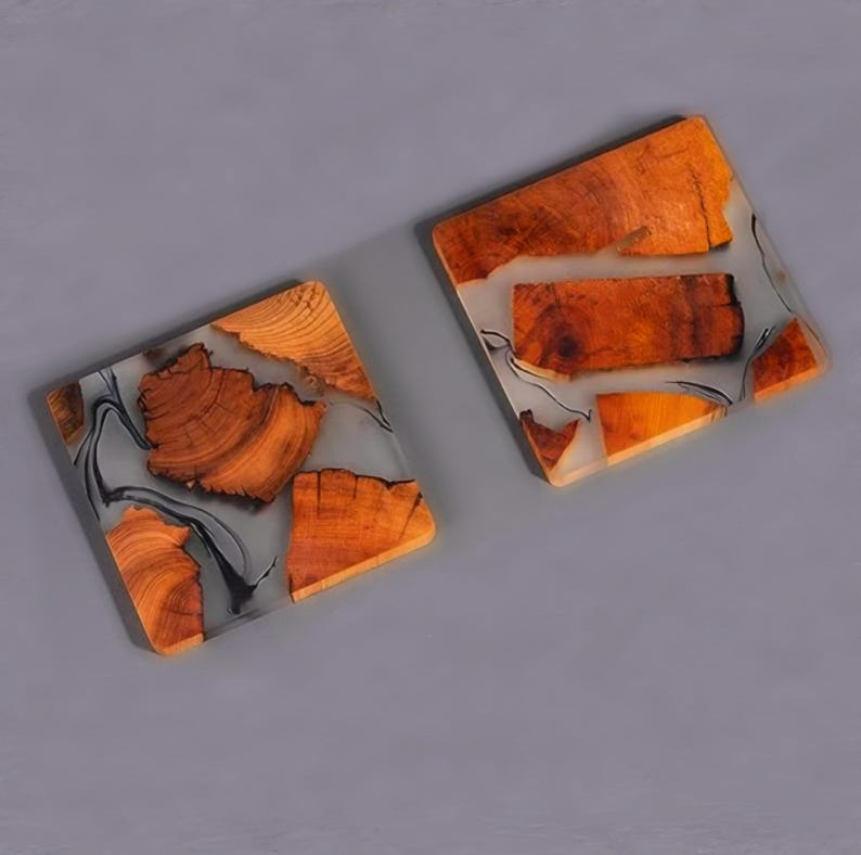 Op de afbeelding: Twee vierkante onderzetters gemaakt van hout en hars. De onderzetters hebben een lichtgrijze harsbasis met ingebedde bruine houten stukken. De houten stukken hebben een natuurlijke houtnerf.