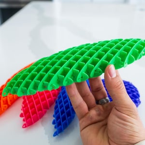 May include: Four colorful, flexible, dome-shaped objects made of plastic. The domes are in shades of green, orange, pink, and blue.