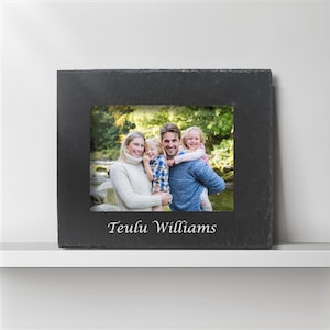 May include: A black slate picture frame with a family photo inside. The photo shows a family of four posing outdoors. The frame has the name "Teulu Williams" engraved at the bottom.
