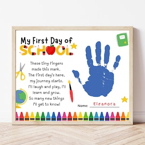 Può includere: Una stampa rettangolare intitolata My First Day of School con un'impronta di mano blu, una poesia, un mappamondo, forbici, un pennello, un quaderno e un bordo di pastelli colorati. Il nome Eleanora è scritto in rosso su una linea nera.