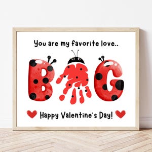 Op de afbeelding: Een ingelijste Valentijnsdag print met het woord "B♥G" in rode letters met een lieveheersbeestjesthema. De letters "B" en "G" hebben zwarte stippen. De letter "B" is gemaakt van een handafdruk. De tekst "Je bent mijn favoriete liefde.." en "Fijne Valentijnsdag!" zijn ook opgenomen.