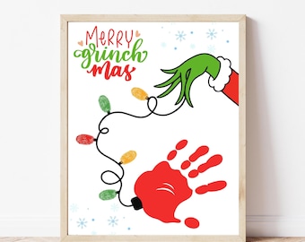 Könnte beinhalten: Ein gerahmter Druck mit weißem Hintergrund zeigt ein Design zum Thema Grinch. Das Kunstwerk umfasst eine grüne Hand, einen roten Handabdruck und eine Lichterkette. Die Worte "Merry Grinchmas" sind in Grün und Rot geschrieben.