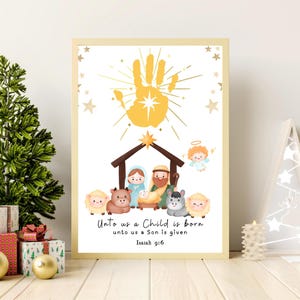 May include: A framed print with a Christmas theme. The artwork features a nativity scene with a handprint and the text "Unto us a Child is born, unto us a Son is given, Isaiah 9:6." The print has a gold frame and is decorated with stars.