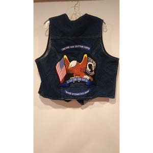 Könnte beinhalten: Eine dunkelblaue Jeansweste mit einem großen gestickten Aufnäher auf der Rückseite. Der Aufnäher zeigt einen Weißkopfseeadler, eine amerikanische Flagge und den Text Lonesome Dove Equestrian Center, POW-MIA, All Gave Some-Some Gave All und Where Veterans Ride Again.