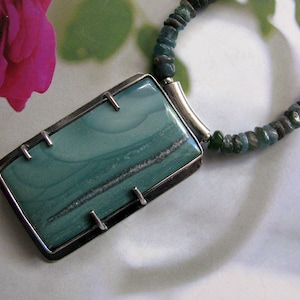 May include: A silver necklace with a rectangular pendant featuring a green and grey stone. The stone has a swirling pattern and is set in a silver frame.