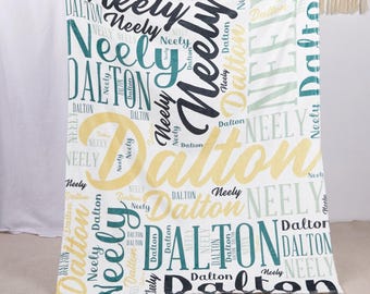 May include: A white blanket with the names "Neely" and "Dalton" in various colors and fonts. The blanket has a repeating pattern of the names in teal, black, and gold. The blanket is soft and cozy.