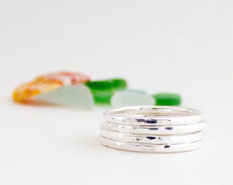 May include: A set of four silver hammered stacking rings. The rings are stacked on top of each other and are in focus. The background is out of focus and is a light white colour.