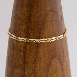 May include: A gold chain necklace with a delicate, double-layered design. The chain is made of small, flat, oval-shaped links.