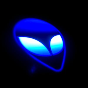 May include: A glowing blue alien head silhouette against a black background. The alien's eyes and outline are illuminated with a bright, electric blue, creating a striking contrast against the darkness.