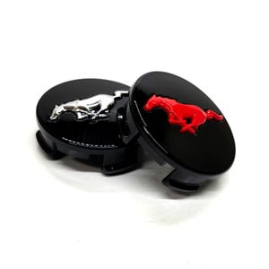 Puede incluir: Tres tapacubos negros con acabado brillante. Dos tapas presentan un emblema de caballo plateado corriendo, mientras que la tercera tiene un emblema de caballo rojo corriendo. Las tapas están diseñadas para uso automotriz.