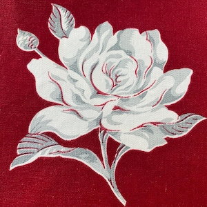 May include: A close-up of a red fabric with a large white rose print. The rose has gray shading and red outlines, with a bud and leaves. The background is a solid, deep red.