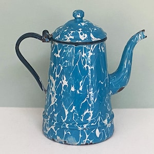 May include: A vintage blue and white enamelware coffee pot with a lid and handle. The pot has a classic speckled pattern and a curved spout. The handle is dark blue. This antique kitchenware is a charming addition to any home.