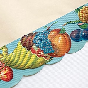 Op de afbeelding: Een lichtblauw geschulpt lint met een bedrukte hoorn des overvloeds vol met diverse vruchten, waaronder een rode appel, een schijfje watermeloen, donkerblauwe druiven, een oranje perzik, een ananas en verschillende donkerpaarse pruimen.