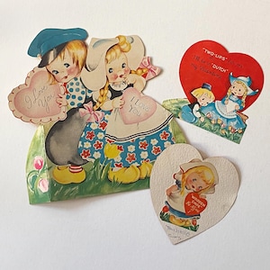 May include: A collection of vintage Valentine's Day cards with Dutch-themed illustrations. The cards depict children in traditional attire, holding heart-shaped messages. One card reads "Two-Lips" and "I'll be in Dutch my Valentine."