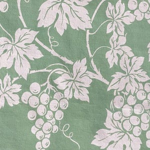 May include: Close-up of a fabric featuring a repeating pattern of white grape clusters and leaves on a pale green backdrop. The design includes detailed vines and tendrils, creating a natural, botanical theme.