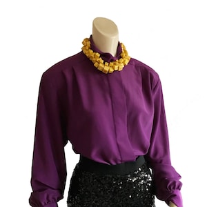 May include: A purple blouse with long sleeves and a high collar. The blouse is paired with a black sequined skirt.