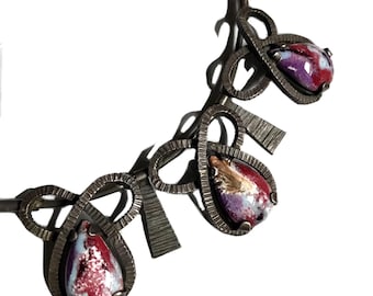May include: A silver necklace with three teardrop-shaped pendants. The pendants are made of glass and have a colorful, abstract design with shades of red, purple, and white.