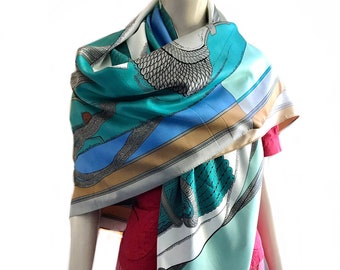 May include: A turquoise, blue, and beige silk scarf with a geometric pattern and a stylized bird design. The scarf is draped around a mannequin.