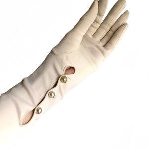 May include: A pair of long, white gloves with pearl buttons. The gloves are made of a smooth, silky fabric.