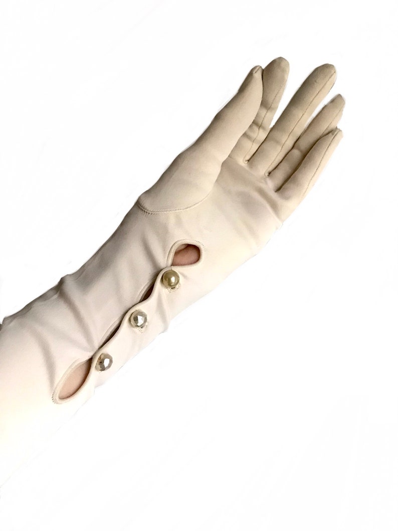 May include: A pair of long, white gloves with pearl buttons. The gloves are made of a smooth, silky fabric.