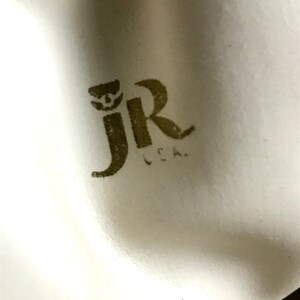 May include: Close-up of a white surface with a brown "JR" logo and the text "L.C.A."