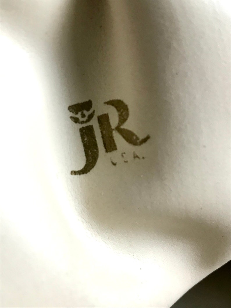 May include: Close-up of a white surface with a brown "JR" logo and the text "L.C.A."