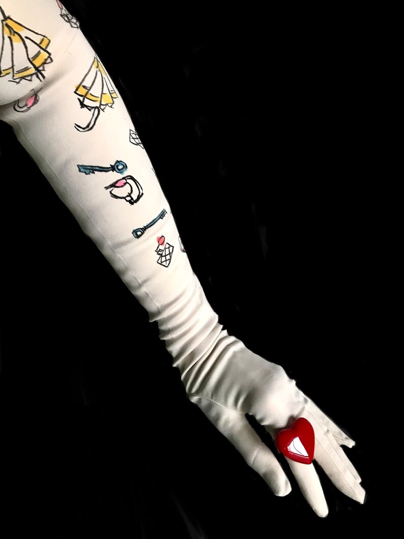 May include: A white long glove with a red heart-shaped ring on the finger. The glove has a pattern of keys, umbrellas, and other small drawings.