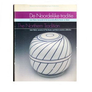 May include: A white ceramic lidded jar with a blue and white striped design. The jar is on a white background. The text on the cover reads "De Noordelijke traditie" and "The Northern Tradition".