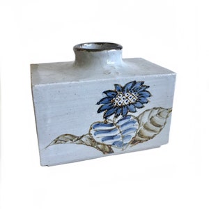 May include: A white ceramic vase with a rectangular shape and a blue and brown sunflower design.