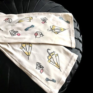 May include: Two white fabric tea towels with a black background. The towels have a repeating pattern of yellow umbrellas, keys, and pink circles.