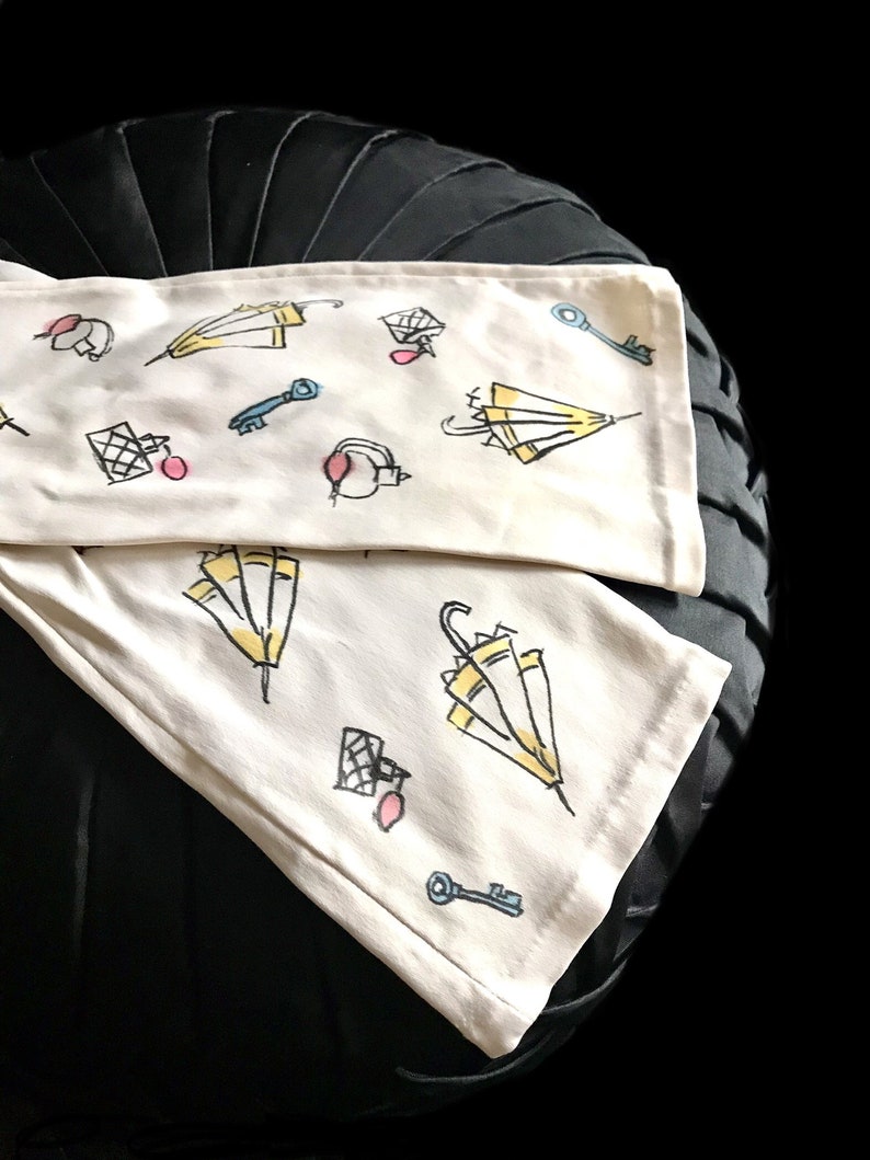 May include: Two white fabric tea towels with a black background. The towels have a repeating pattern of yellow umbrellas, keys, and pink circles.