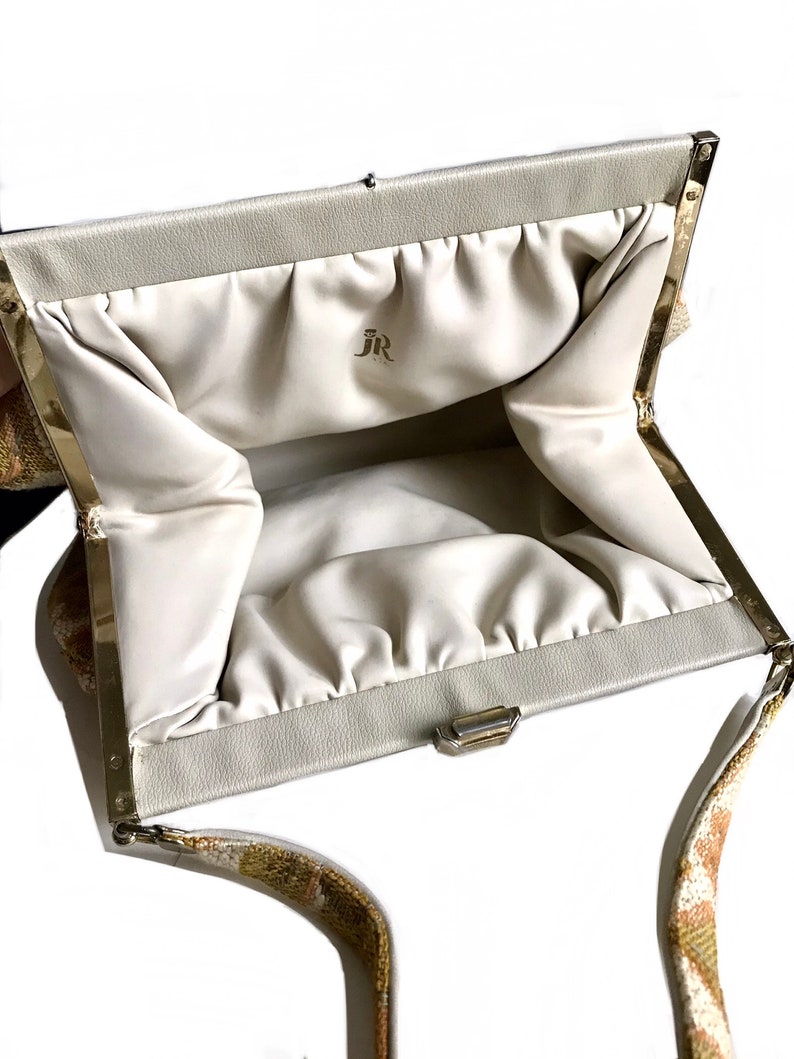 May include: A white clutch bag with a gold clasp and a gold chain strap. The bag has a white satin lining and the initials "JR" are printed on the inside.