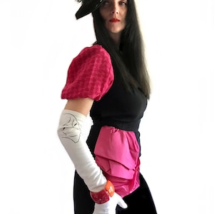May include: A woman wearing a black dress with a pink ruffled skirt, a black hat with a feather, and white gloves. She is wearing a pink and white patterned blouse with puffed sleeves.